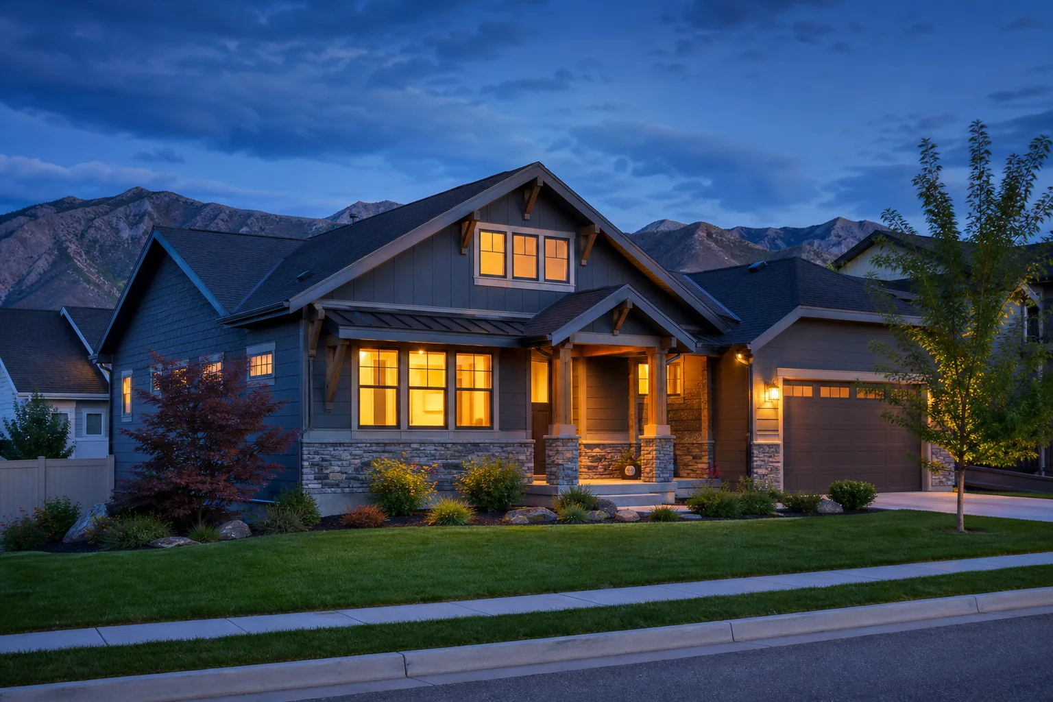 A comfortable Utah home with warm lights at blue hour and the Wasatch mountains beyond